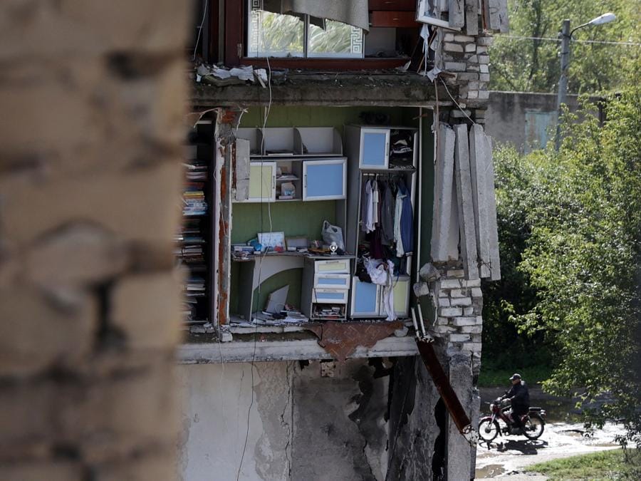 Un uomo guida una moto nei pressi di un edificio residenziale distrutto nella città di Izyum. (Photo by Anatolii Stepanov / AFP)