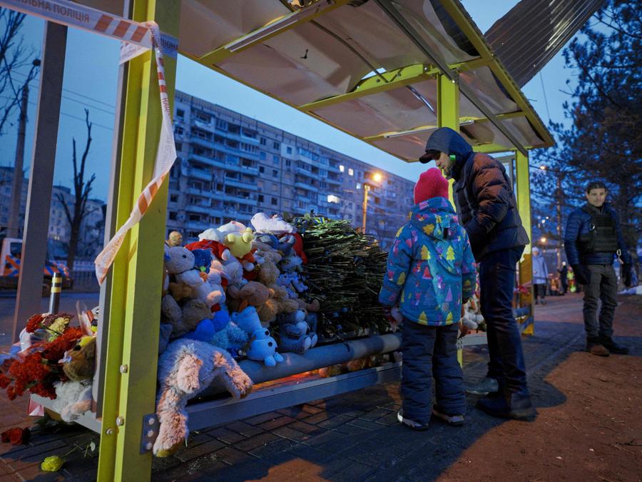 La gente mette fiori e giocattoli a una fermata dell’autobus di fronte a un edificio residenziale nella città ucraina di Dnipro, distrutta a seguito di un attacco missilistico. (Photo by Vitalii Matokha / AFP)
