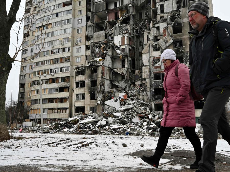 Un uomo e una donna passano davanti a un condominio, parzialmente distrutto dai bombardamenti, nella città ucraina di Kharkiv. (Photo by SERGEY BOBOK / AFP)