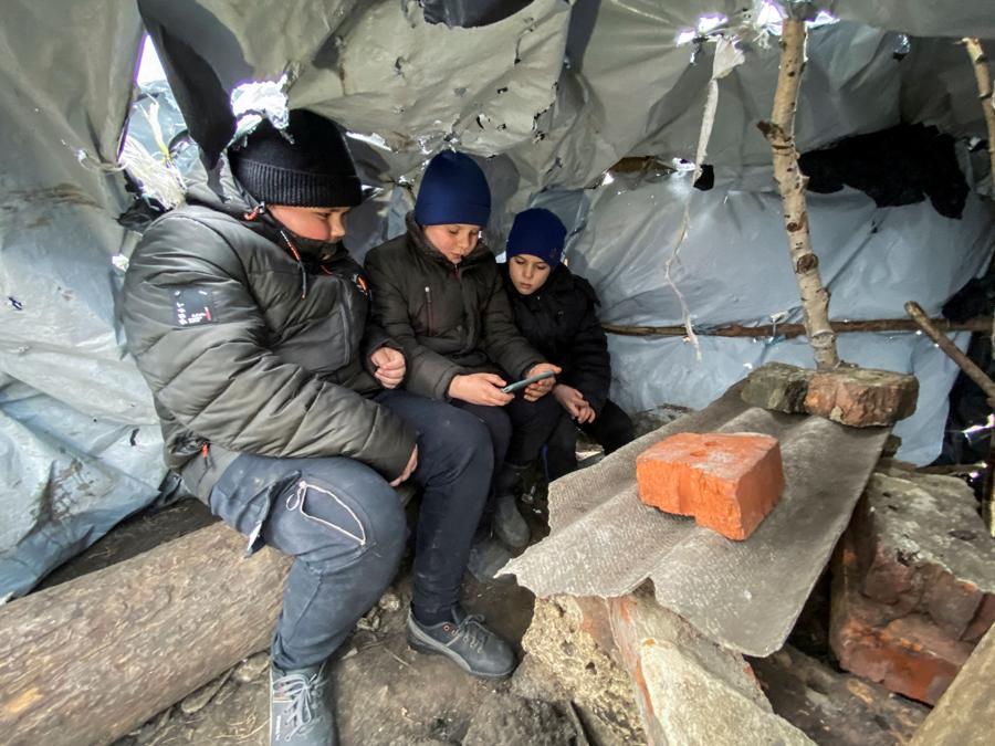 Tre ragazzini frequentano una lezione online in un’aula improvvisata costruita da loro con pali di legno e teli di plastica sull’unica collina del villaggio che riceve Internet mobile, nel villaggio di Hontarivka, nella regione di Kharkiv. (REUTERS/Vitalii Hnidyi)