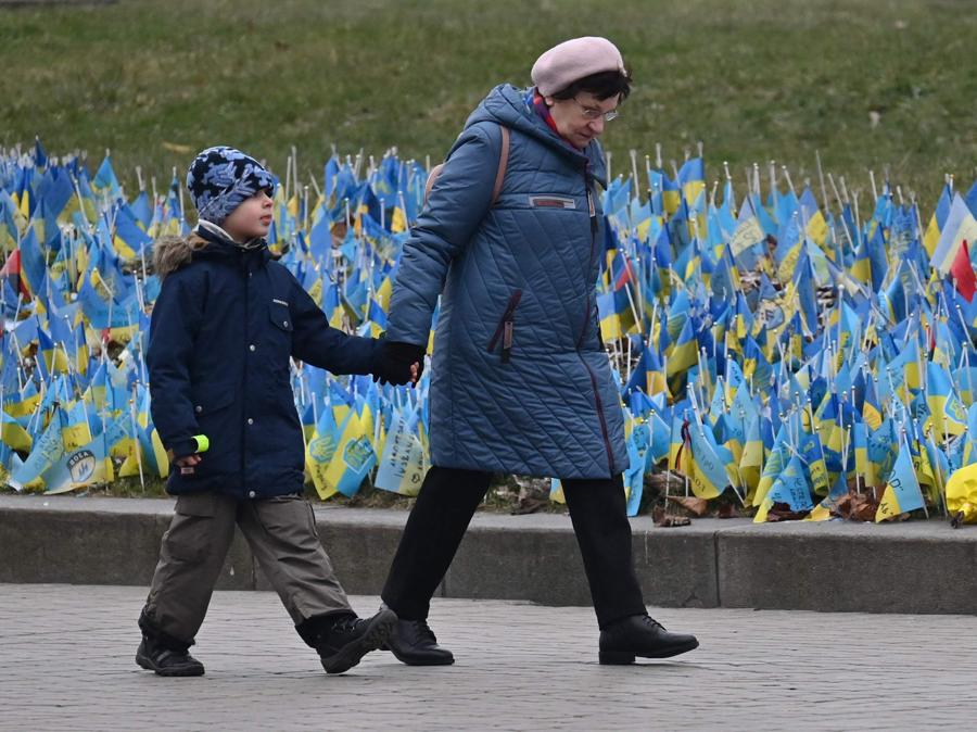Una donna cammina con un bambino davanti alle bandiere ucraine che simboleggiano coloro che sono morti durante l’invasione russa dell’Ucraina, in Piazza dell’Indipendenza di Kiev. (Photo by Sergei Supinsky / AFP)