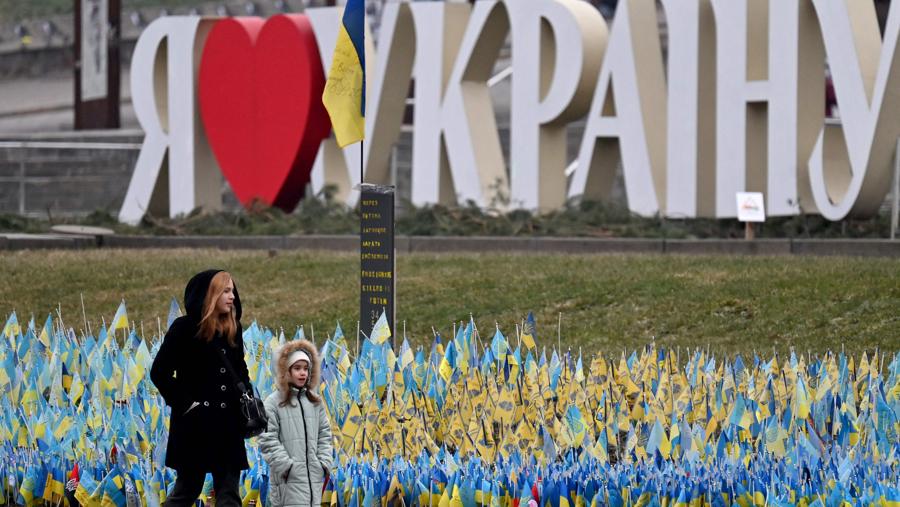 Una donna e una bambina camminano davanti alle bandiere ucraine che simboleggiano coloro che sono morti durante l’invasione russa dell’Ucraina, in Piazza dell’Indipendenza a Kiev. (Photo by Sergei Supinsky / AFP)
