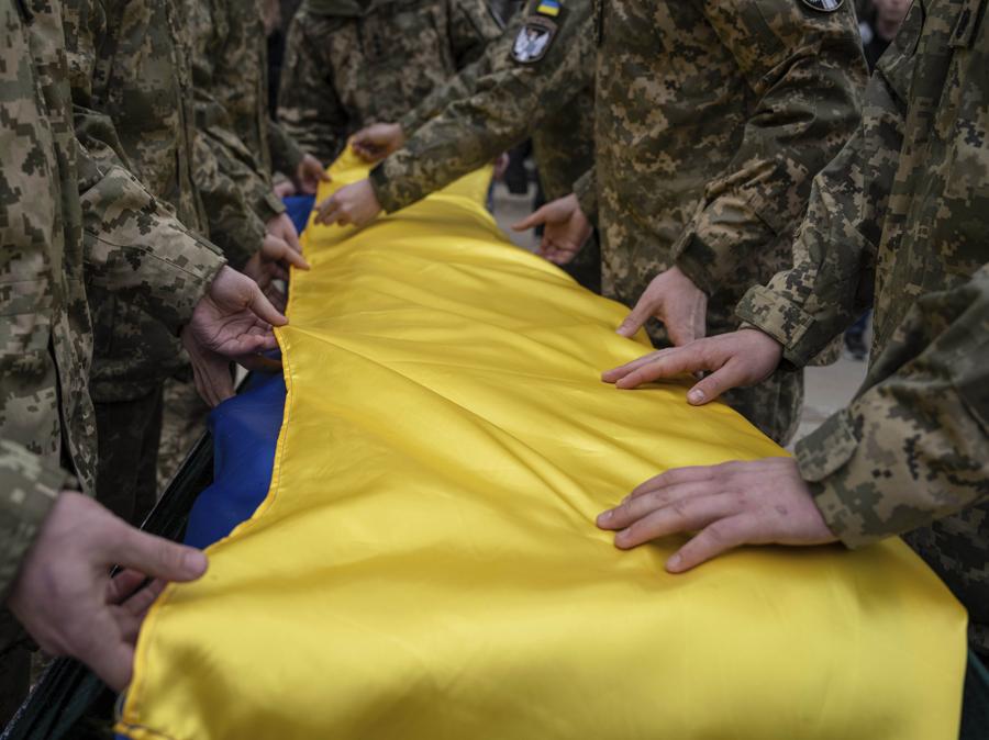 I militari ucraini piegano la bandiera nazionale sulla bara del loro compagno Andrii Neshodovskiy durante la cerimonia funebre a Kiev. (AP Photo/Evgeniy Maloletka)