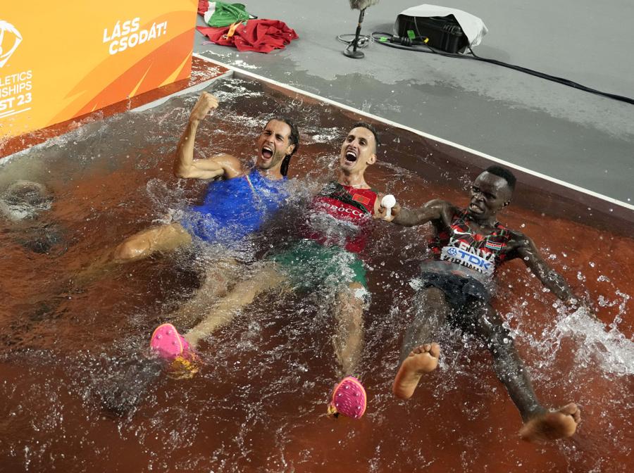 Gianmarco Tamberi, italiano, a sinistra, Soufiane El Bakkali, del Marocco, al centro, e Abraham Kibiwot, del Kenya, festeggiano nella vasca della corsa a ostacoli durante i Campionati mondiali di atletica di Budapest. Tamberi ha vinto la finale del salto in alto maschile, El Bakkali vince i 3000 metri siepi maschili e Kibiwot arriva terzo. (AP Photo/Ashley Landis)