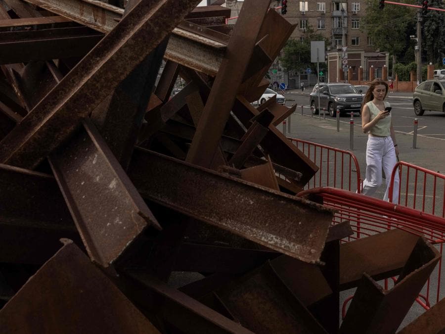 Una donna passa davanti a un mucchio di barriere di metallo per carri armati nel centro di Kiev. (Photo by Roman PILIPEY / AFP)