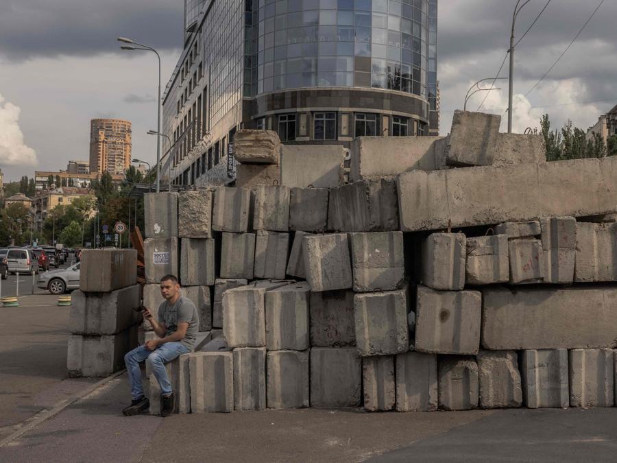 Un uomo siede accanto a blocchi di cemento, raccolti dai posti di blocco militari, nel centro di Kiev. (Photo by Roman PILIPEY / AFP)