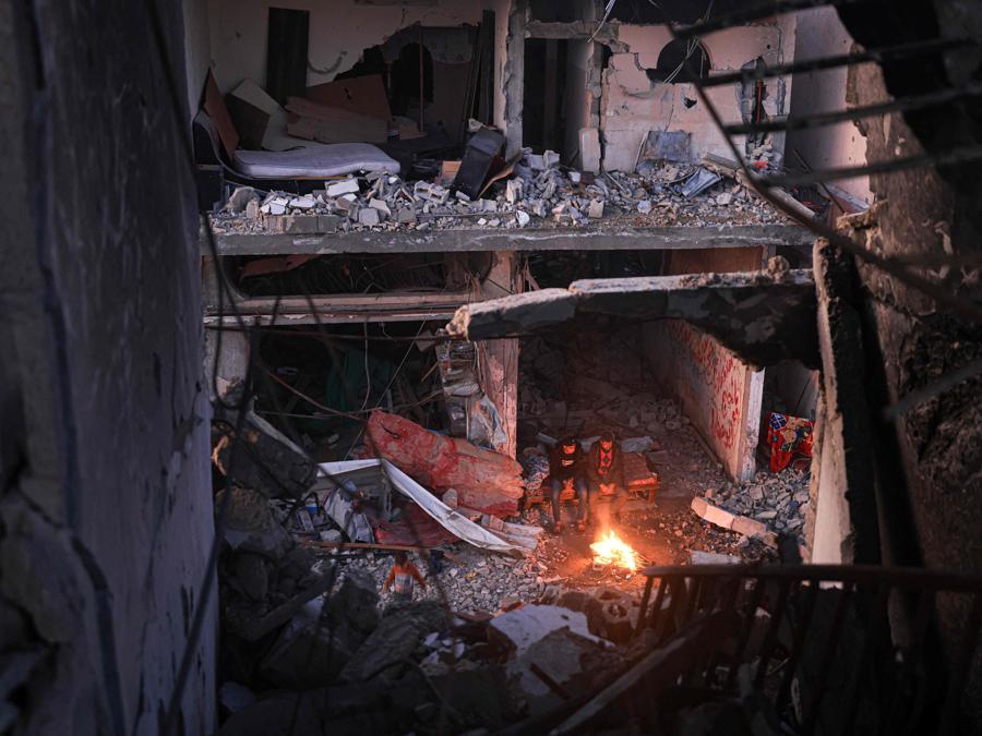 Le persone si siedono attorno a un fuoco da campo in mezzo agli edifici distrutti nel distretto di Khezaa, alla periferia della città di Khan Yunis, nel sud della Striscia di Gaza. (Photo by Mahmud HAMS / AFP)