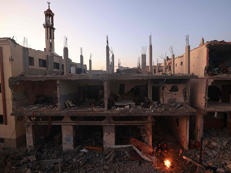 Le persone si siedono attorno a un fuoco da campo in mezzo agli edifici distrutti nel distretto di Khezaa, alla periferia della città di Khan Yunis, nel sud della Striscia di Gaza. (Photo by Mahmud HAMS / AFP)