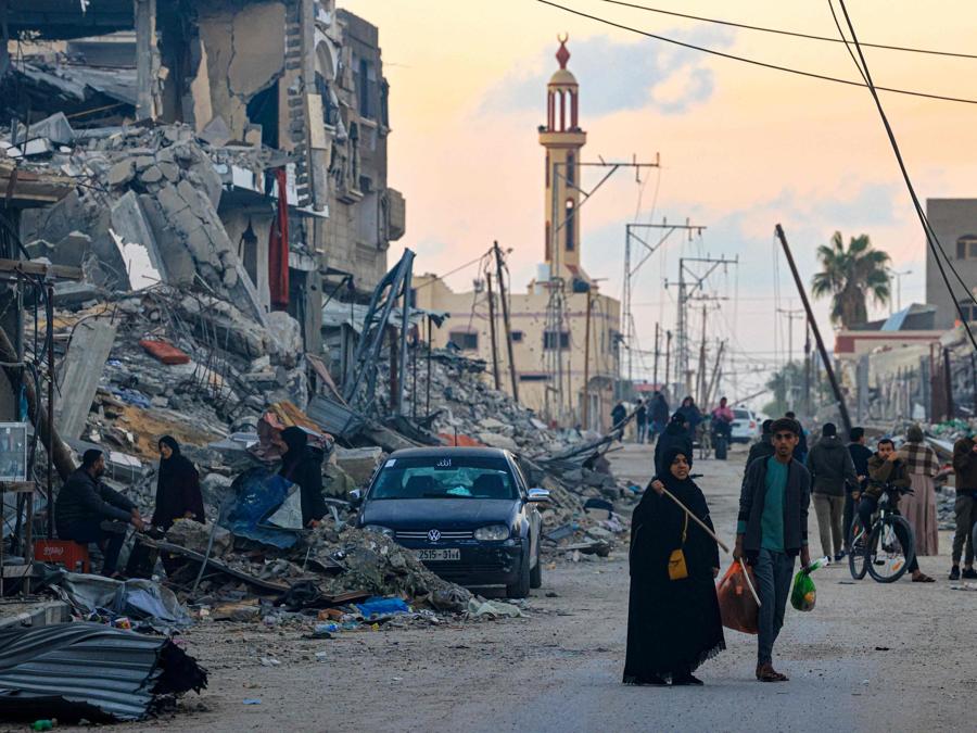La gente cammina lungo una strada nel distretto di Khezaa, alla periferia della città di Khan Yunis, nel sud della Striscia di Gaza. (Photo by MAHMUD HAMS / AFP)