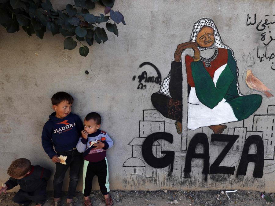 Bambini palestinesi sfollati stanno accanto a un dipinto murale dell’artista Amal Abo a Rafah, nel sud della Striscia di Gaza. (Photo by AFP)