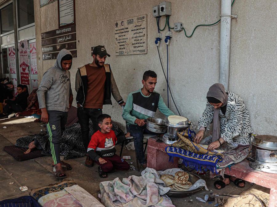Giovani restano a guardare mentre un uomo e una donna preparano il cibo in un campo che ospita palestinesi sfollati fuori dall’ospedale europeo di Khan Yunis, nel sud della Striscia di Gaza. (Photo by AFP)