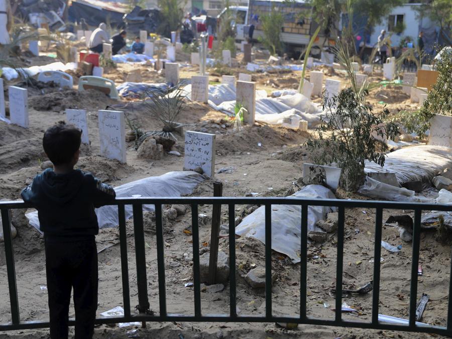 Un bambino palestinese guarda le tombe delle persone uccise nel bombardamento israeliano della Striscia di Gaza e sepolte all’interno dell’ospedale Shifa nella città di Gaza. (AP Photo/Mohammed Hajjar)