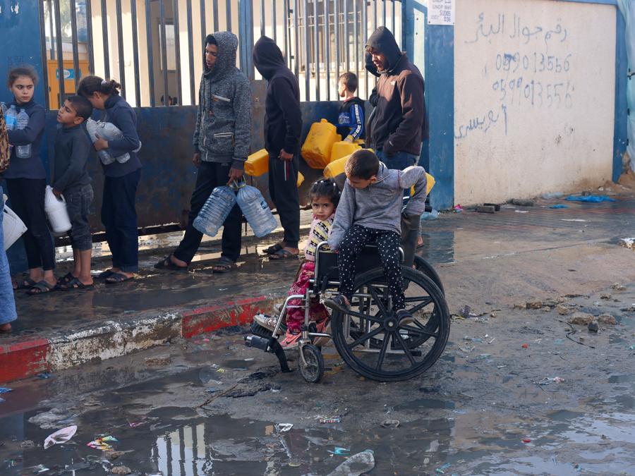 Bambini palestinesi seduti su una sedia a rotelle mentre le persone fanno la fila per raccogliere l’acqua, a Rafah, nel sud della Striscia di Gaza. REUTERS/Saleh Salem