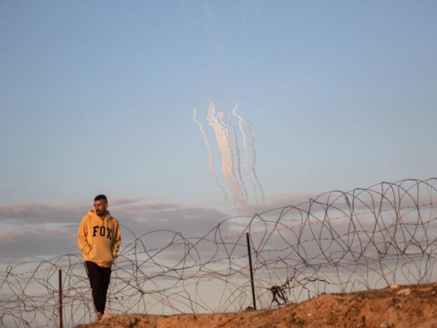 Razzi vengono lanciati dalla Striscia di Gaza (sullo sfondo) mentre un palestinese sfollato cammina vicino al confine palestinese-egiziano nel campo di Rafah, nel sud della Striscia di Gaza. EPA/HAITHAM IMAD