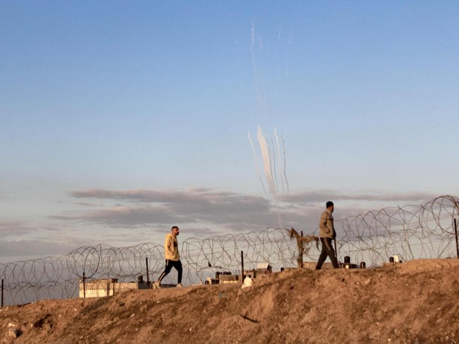 Razzi vengono lanciati dalla Striscia di Gaza (sullo sfondo) mentre palestinesi sfollati camminano vicino al confine palestinese-egiziano nel campo di Rafah, nel sud della Striscia di Gaza. EPA/HAITHAM IMAD