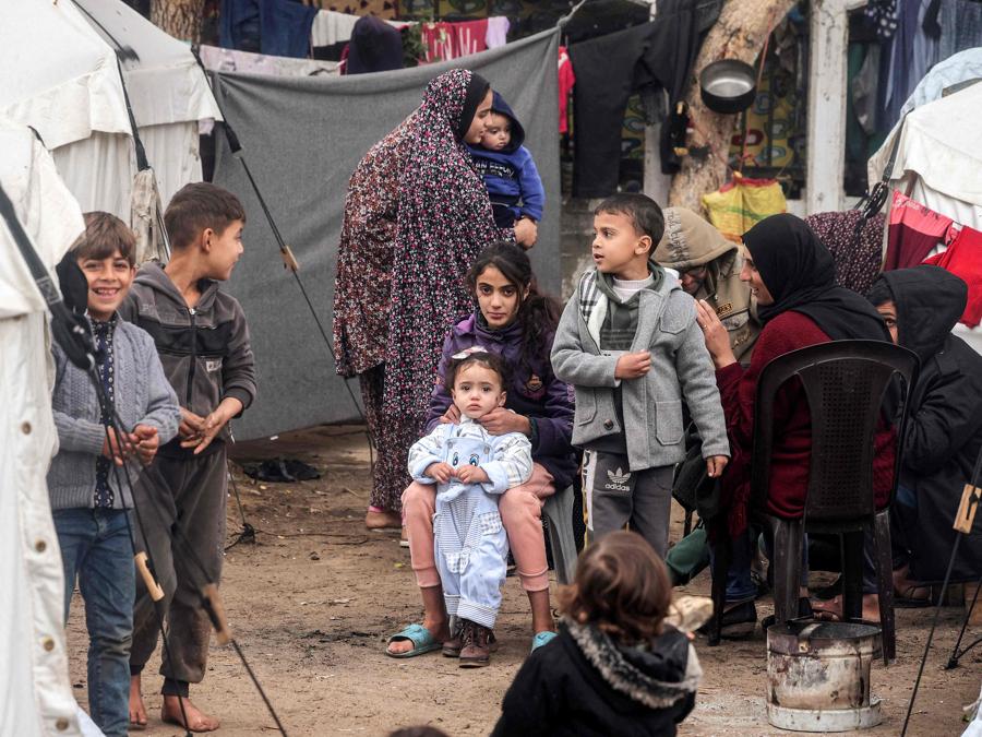 Donne e bambini sono fotografati lungo un vicolo tra le tende in un campo improvvisato per sfollati palestinesi a Rafah, nel sud della Striscia di Gaza. (Photo by AFP)