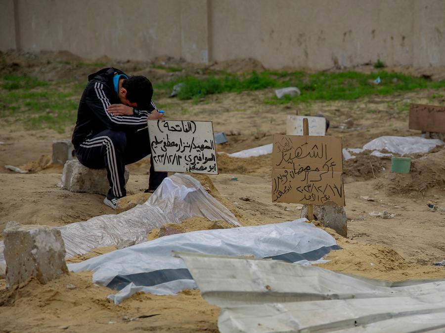 Un giovane siede accanto alla tomba di una persona uccisa dai bombardamenti israeliani mentre i corpi vengono allineati in un cimitero improvvisato in un quartiere residenziale vicino al distretto al-Shabiyah di Gaza City. (Photo by AFP)