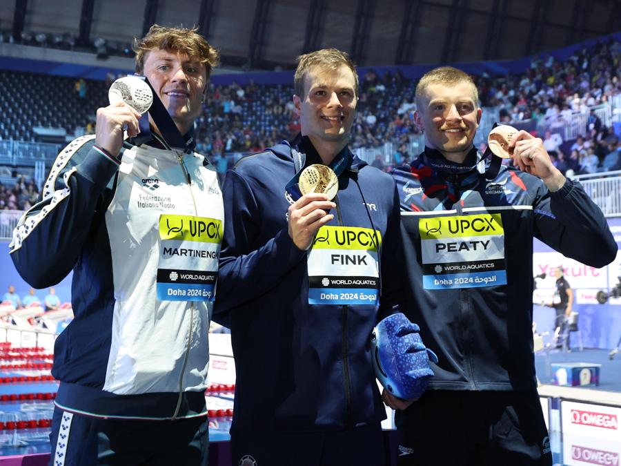 12 febbraio 2024 - Sul podio da sinistra: la medaglia d’argento Nicolo Martinenghi dell’Italia, la medaglia d’oro Nic Fink degli Stati Uniti e la medaglia di bronzo Adam Peaty della Gran Bretagna posano durante la cerimonia di premiazione per i 100 metri a rana maschili ai Campionati mondiali di nuoto FINA Doha 2024. (EPA/Ali Haider)
