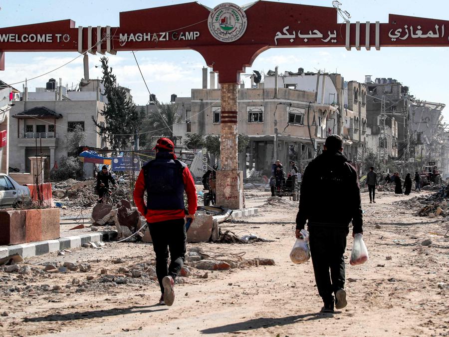 Le persone attraversano il cancello del campo di Maghazi per rifugiati palestinesi, gravemente danneggiato dai bombardamenti israeliani. (Photo by ANAS BABA / AFP)