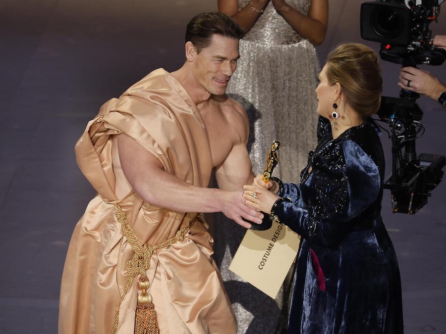 John Cena (a sinistra) consegna l’Oscar a Holly Waddington (a destra) dopo aver vinto il premio per i migliori costumi durante la 96esima cerimonia annuale degli Academy Awards al Dolby Theatre nel quartiere Hollywood di Los Angeles, California. (EPA/Caroline Brehman)