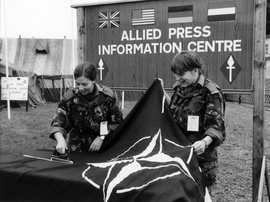 Due soldatesse britanniche stirano una bandiera della NATO davanti all’Allied Press Information Center di Hildesheim il 19 settembre 1984. (Photo by DPA / DPA / dpa Picture-Alliance via AFP)