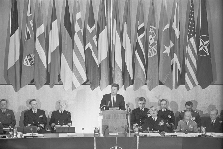 Kennedy si rivolge ai capi della NATO. Washington: il presidente Kennedy si rivolge  a una riunione dei capi militari dei paesi dell’Organizzazione del Trattato del Nord Atlantico  al Dipartimento di Stato. Ha promesso di mantenere le forze statunitensi in Europa e di rafforzare la loro capacità di guerra convenzionale. Seduti a destra, davanti ci sono il conte Mountbatten, d’Inghilterra, presidente del comitato militare (a sinistra) e il generale Adolf Heusinger, dell’esercito tedesco. 10 aprile 1961 (Getty Images)
