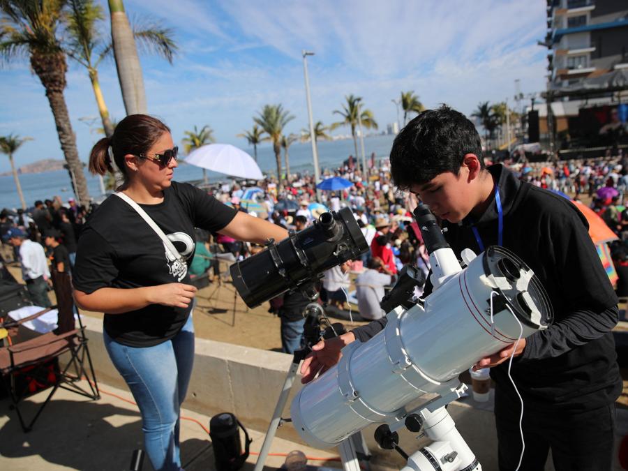 Un giovane e una donna preparano i loro telescopi mentre le persone si riuniscono e aspettano di osservare un’eclissi solare totale a Mazatlan, in Messico. REUTERS/Henry Romero
