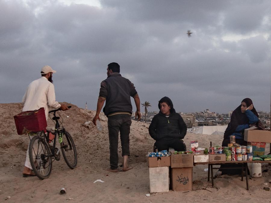 Persone passano davanti alla bancarella di cibo di una famiglia palestinese sfollata sulla spiaggia nel campo profughi di Rafah, nel sud della Striscia di Gaza. EPA/HAITHAM IMAD
