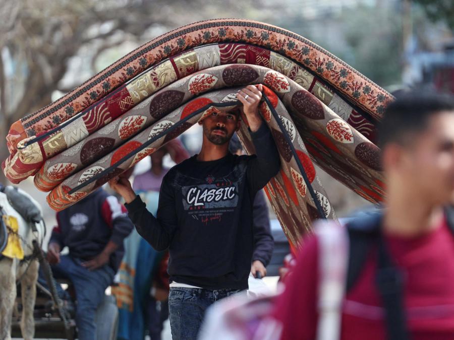 Un uomo palestinese trasporta materassi mentre le persone lasciano le loro case con le loro cose nel campo profughi di Nuseirat, nel centro di Gaza. (Photo by AFP)