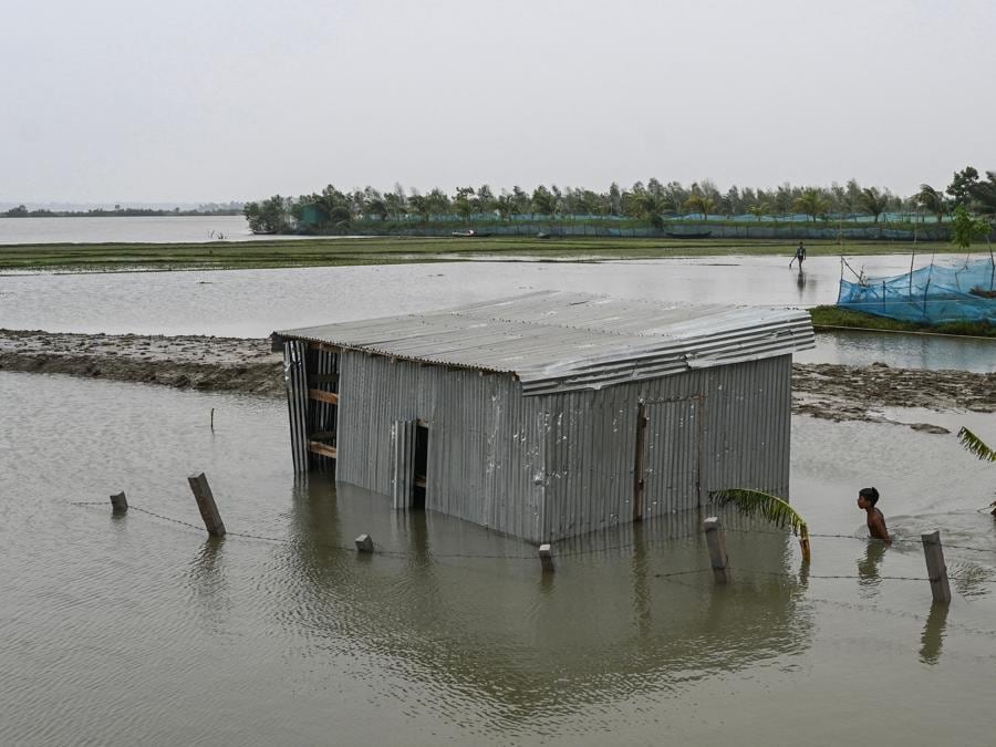 Un ragazzo passa davanti a una casa parzialmente sommersa dopo le forti piogge a Patuakhali il 28 maggio 2024, in seguito all’atterraggio del ciclone Remal in una zona bassa del Bangladesh. Il ciclone Remal, che si è abbattuto sulle pianure del Bangladesh e sulla vicina India la sera del 26 maggio con violente tempeste e onde che si infrangono, ha provocato la morte di almeno 38 persone, distrutto migliaia di case, distrutto dighe marine e allagato città nei due paesi. (Photo by MUNIR UZ ZAMAN / AFP)