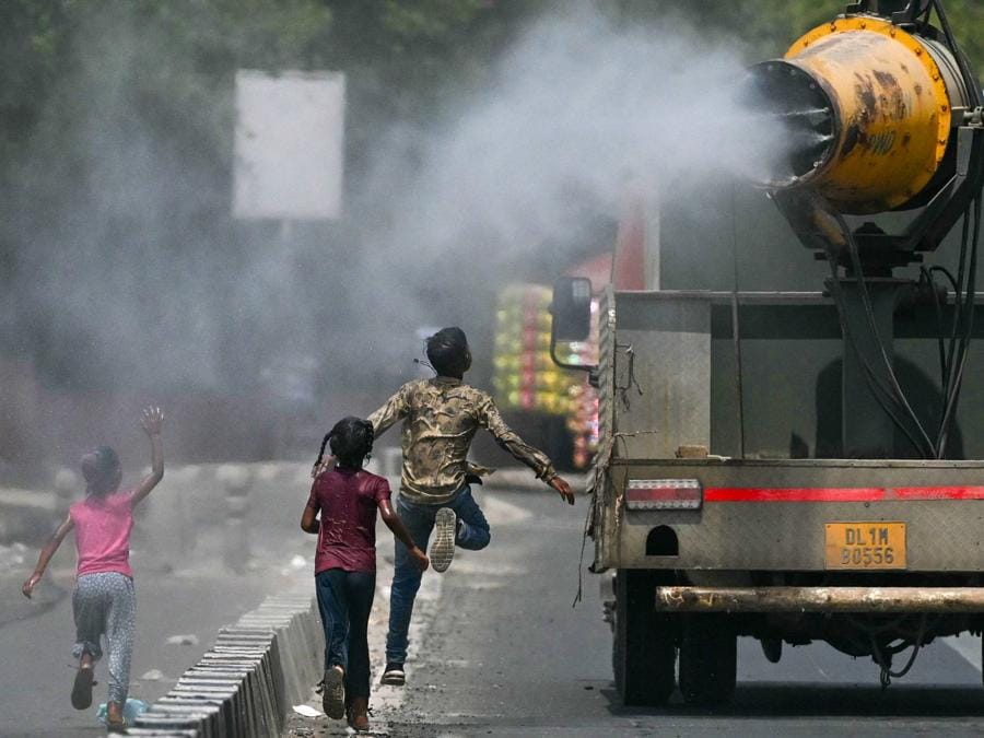 Bambini corrono dietro un camion spruzzando acqua lungo una strada in una calda giornata estiva a Nuova Delhi. (Photo by Arun SANKAR / AFP)