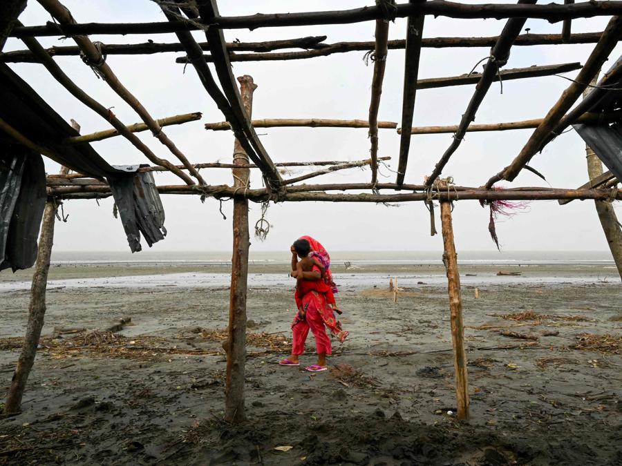 Una donna porta con sé un bambino mentre passa davanti a un negozio danneggiato dopo l’abbattimento del ciclone Remal a Patuakhali. Il ciclone Remal, che si è abbattuto sulle pianure del Bangladesh e sulla vicina India la sera del 26 maggio con violente tempeste e onde che si infrangono, ha provocato la morte di almeno 38 persone, distrutto migliaia di case, distrutto dighe marine e allagato città nei due paesi. (Photo by Munir Uz Zaman / AFP)