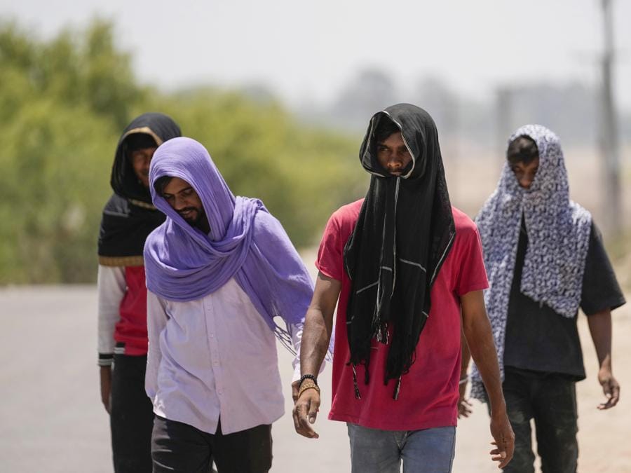 Le persone si coprono la testa con sciarpe per proteggersi dal sole cocente in una calda giornata estiva a Jammu. (AP Photo/Channi Anand)
