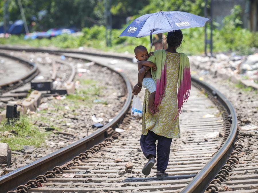 Una donna tiene un ombrello e cammina su un binario ferroviario con un bambino in una calda giornata estiva a Guwahati. (AP Photo/Anupam Nath)