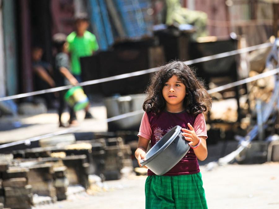 Una giovane ragazza palestinese porta con sé una pentola mentre si dirige verso un punto di donazione di cibo a Nuseirat, nel centro della Striscia di Gaza. (Photo by Eyad BABA / AFP)