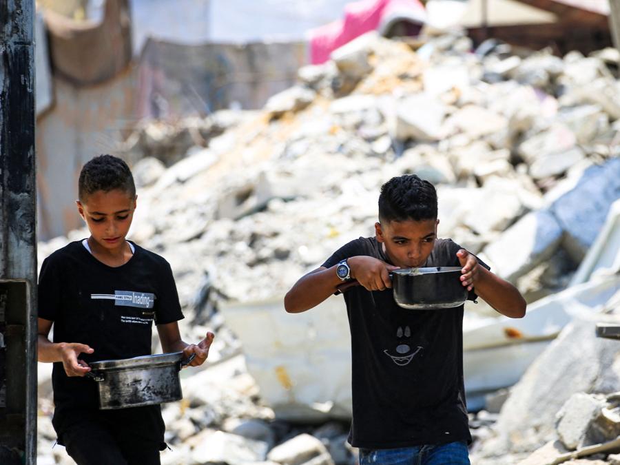 Giovani ragazzi palestinesi trasportano pentole di cibo donato a Nuseirat, nel centro della Striscia di Gaza. (Photo by Eyad BABA / AFP)