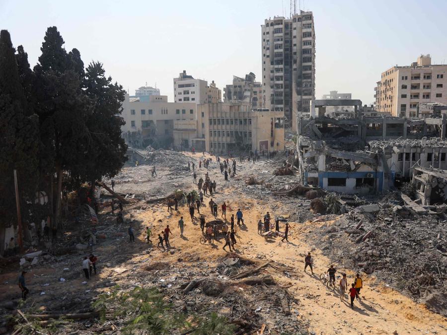 Persone  camminano sulle macerie del complesso edilizio danneggiato dell’Agenzia delle Nazioni Unite per il soccorso e l’occupazione dei rifugiati palestinesi (UNRWA) nel quartiere Al-Sinaa, nella parte occidentale di Gaza City. (Photo by Omar AL-QATTAA / AFP)