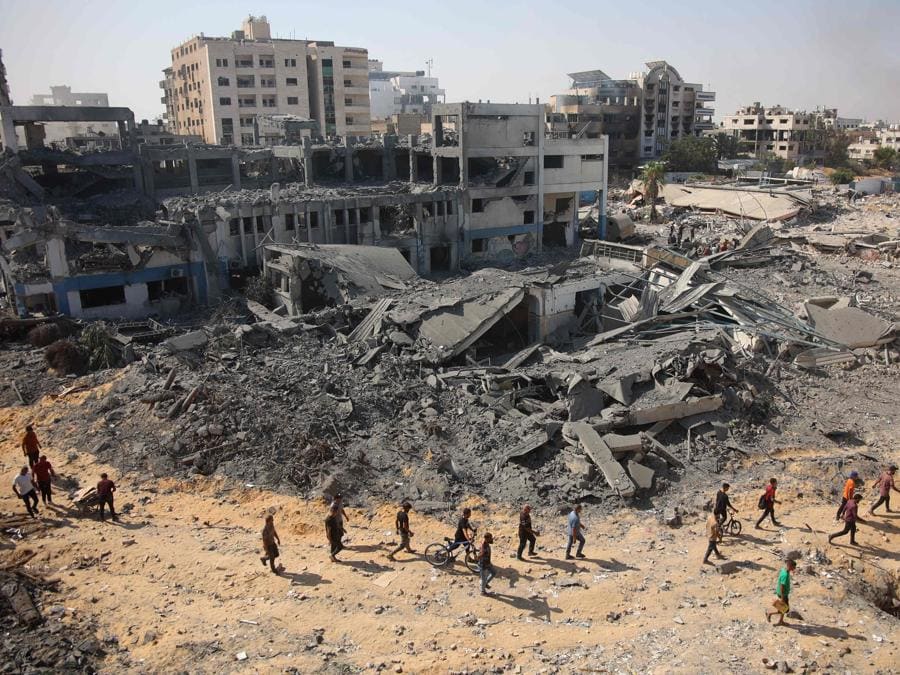 Persone  camminano sulle macerie del complesso edilizio danneggiato dell’Agenzia delle Nazioni Unite per il soccorso e l’occupazione dei rifugiati palestinesi (UNRWA) nel quartiere Al-Sinaa, nella parte occidentale di Gaza City. (Photo by Omar AL-QATTAA / AFP)