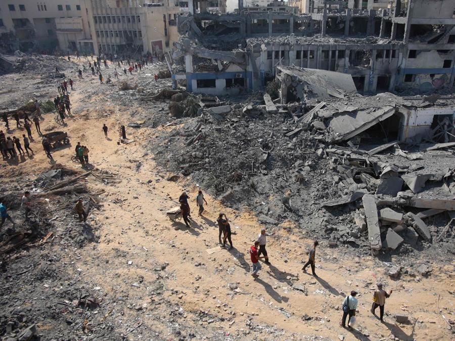 Persone  camminano sulle macerie del complesso edilizio danneggiato dell’Agenzia delle Nazioni Unite per il soccorso e l’occupazione dei rifugiati palestinesi (UNRWA) nel quartiere Al-Sinaa, nella parte occidentale di Gaza City. (Photo by Omar AL-QATTAA / AFP)