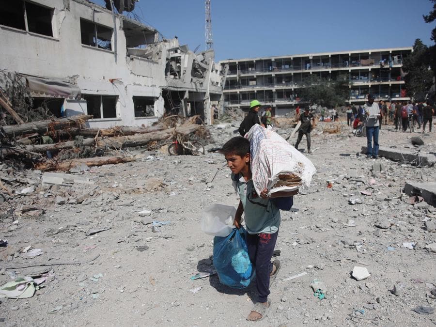 Gli sfollati recuperano oggetti dal complesso edilizio danneggiato dell’Agenzia delle Nazioni Unite per il soccorso e l’occupazione dei rifugiati palestinesi (UNRWA) nel quartiere Al-Sinaa, nella parte occidentale di Gaza City. (Photo by Omar AL-QATTAA / AFP)
