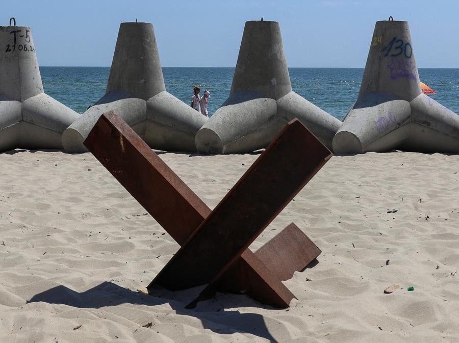Persone camminano vicino ai tetrapodi usati come barriere contro le navi da sbarco militari russe, sulla spiaggia nella città di Chornomorsk, regione di Odessa. (REUTERS/Nina Liashonok)