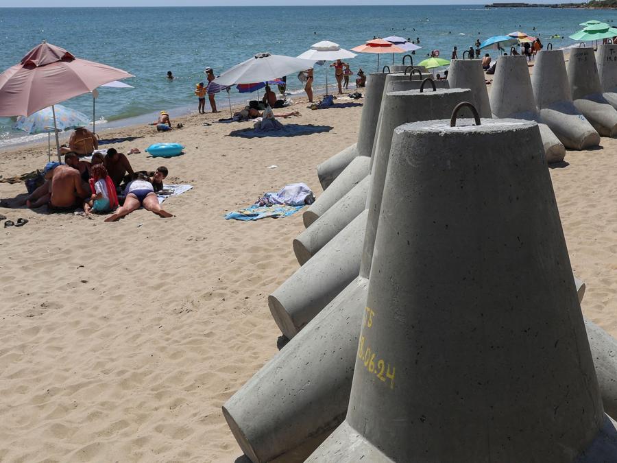 Persone riposano sulla spiaggia vicino a tetrapodi usati come barriere contro le navi da sbarco militari russe,  nella città di Chornomorsk, regione di Odessa. (REUTERS/Nina Liashonok)