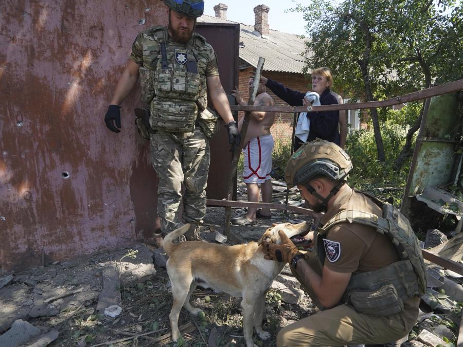 Un agente di polizia calma un cane dopo l’attacco aereo russo sul quartiere residenziale di Bilyi Kolodiaz, regione di Kharkiv. (AP Photo/Andrii Marienko)