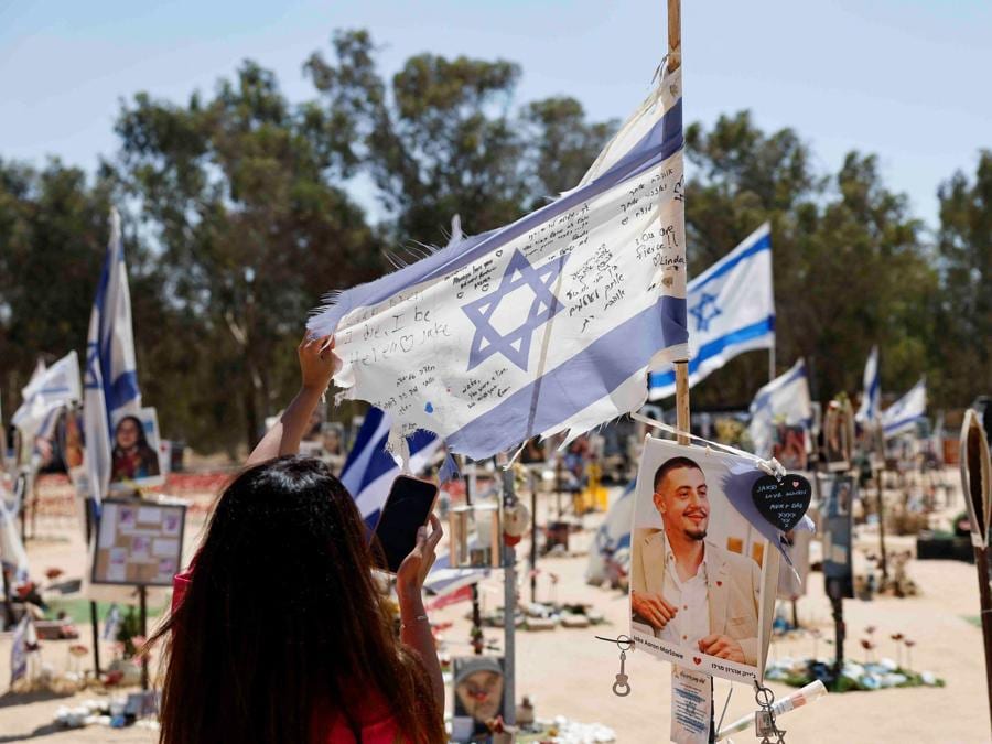 A Reim, nel sud di Israele, una donna tocca una bandiera israeliana nel luogo del Nova festival  dove i partecipanti alla festa sono stati uccisi e rapiti, a 300 giorni dall’attacco mortale del 7 ottobre da parte di uomini armati di Hamas. (REUTERS/Amir Cohen)