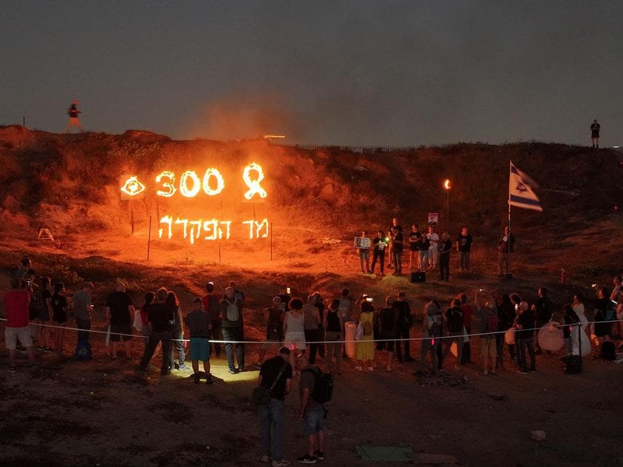 Una ripresa da un drone mostra persone che guardano un cartello infuocato con le parole in ebraico “300 giorni di abbandono” durante un evento a sostegno degli ostaggi tenuti a Gaza in riferimento ai 300 giorni trascorsi dall’attacco mortale del 7 ottobre. (REUTERS/Ilan Rosenberg)