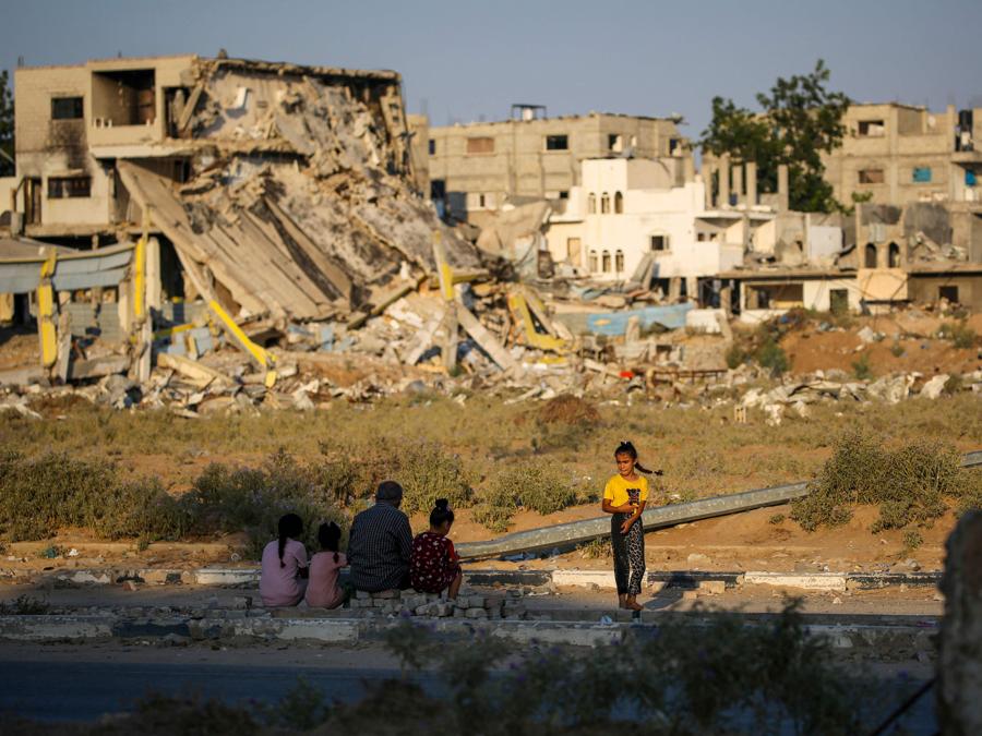 Persone sedute su un marciapiede vicino alle macerie degli edifici distrutti durante i bombardamenti israeliani nel campo profughi palestinese di al-Maghazi, nella Striscia di Gaza centrale. (Photo by Eyad Baba / AFP)