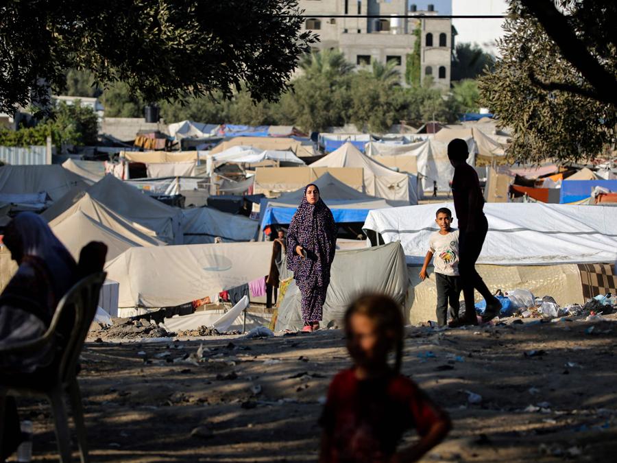 I bambini giocano mentre una donna cammina vicino a rifugi di fortuna nel campo profughi palestinese di al-Maghazi, nella Striscia di Gaza centrale. (Photo by Eyad Baba / AFP)