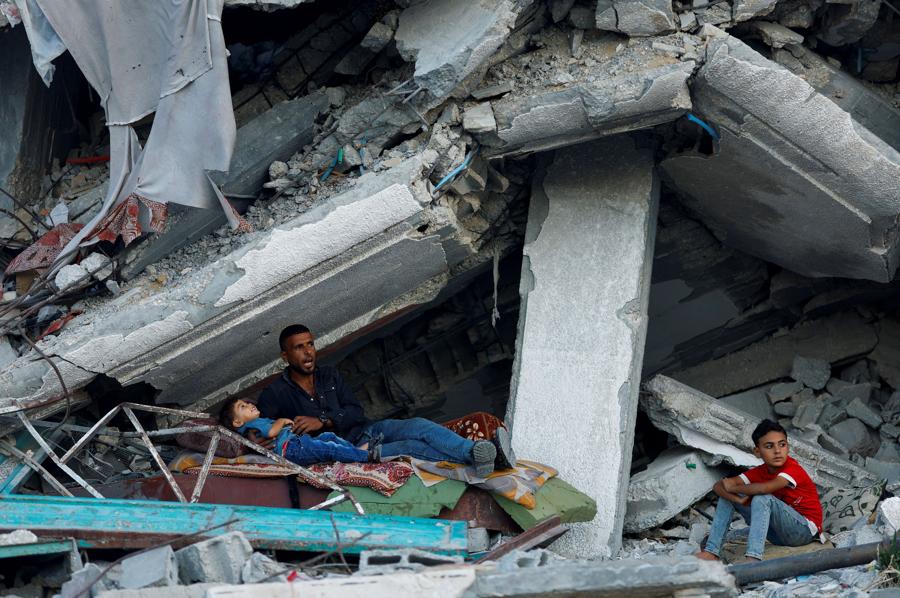 Un uomo palestinese riposa con i figli sotto le macerie di una casa distrutta dagli attacchi israeliani a Khan Younis, nel sud della Striscia di Gaza. (Reuters)
