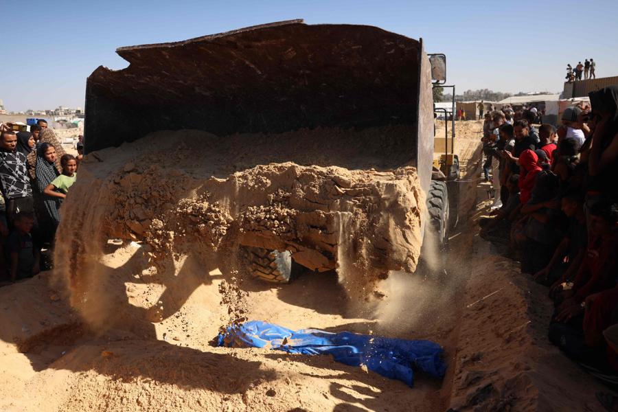 Un escavatore versa la sabbia su uno degli 88 corpi sepolti in una fossa comune a Khan Yunis.  Un camion, che secondo il ministero della Sanità palestinese è entrato nella Striscia di Gaza da Israele il giorno prima, ha trasportato 88 corpi per la sepoltura in una fossa comune a Khan Yunis. (AFP)