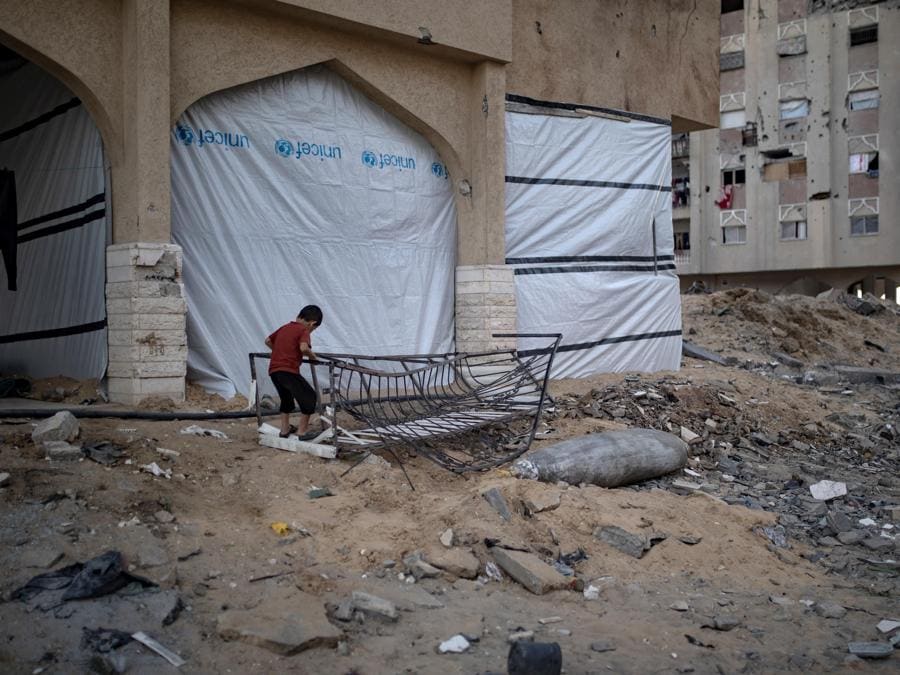 Un bambino palestinese gioca accanto a un missile israeliano inesploso tra le macerie di un edificio distrutto nel campo profughi di Khan Yunis, nel sud della Striscia di Gaza. EPA/HAITHAM IMAD